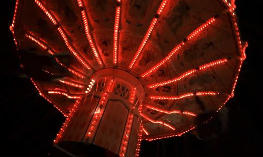 The underside of a carnival swing, glowing red
