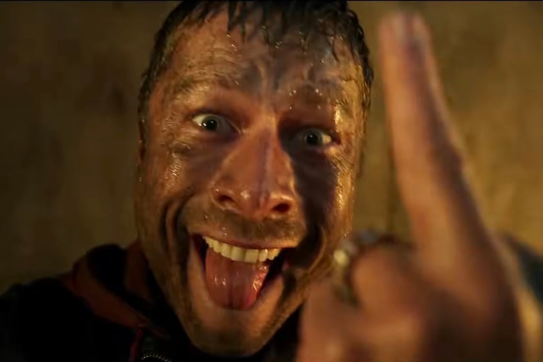 A muddy Glen Powell gives the finger to the audience in The Running Man