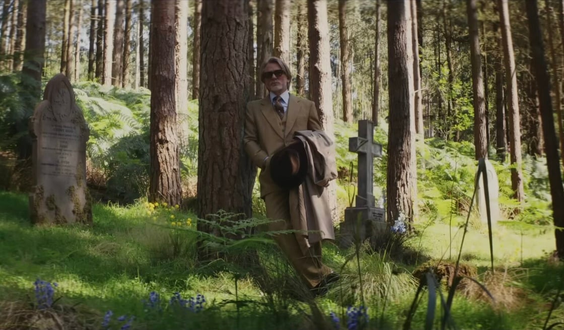 Benoit Blanc standing in a wooded graveyard