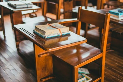 A picture of old-fashioned wooden school desks with small stacks of books