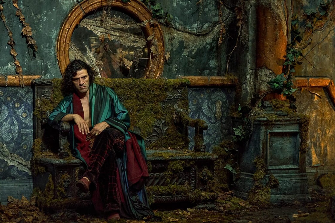 Oscar Isaac pouting on a moss-covered chair