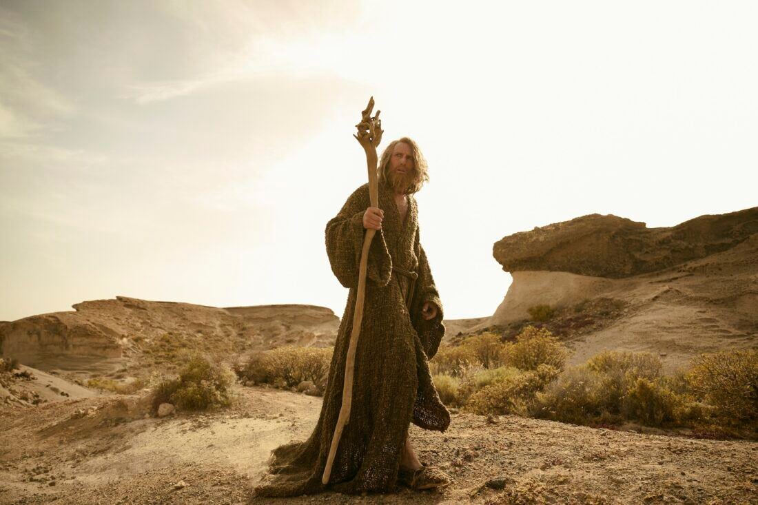 A screencap from The Rings of Power. A younger version of Gandalf stands on a cliff, holding a staff