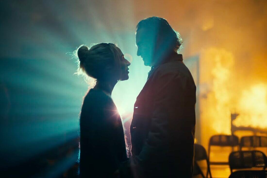 The Joker (Joaquin Phoenix) and Harley Quinn (Lady Gaga) standing silhouetted together, framed by light and fire